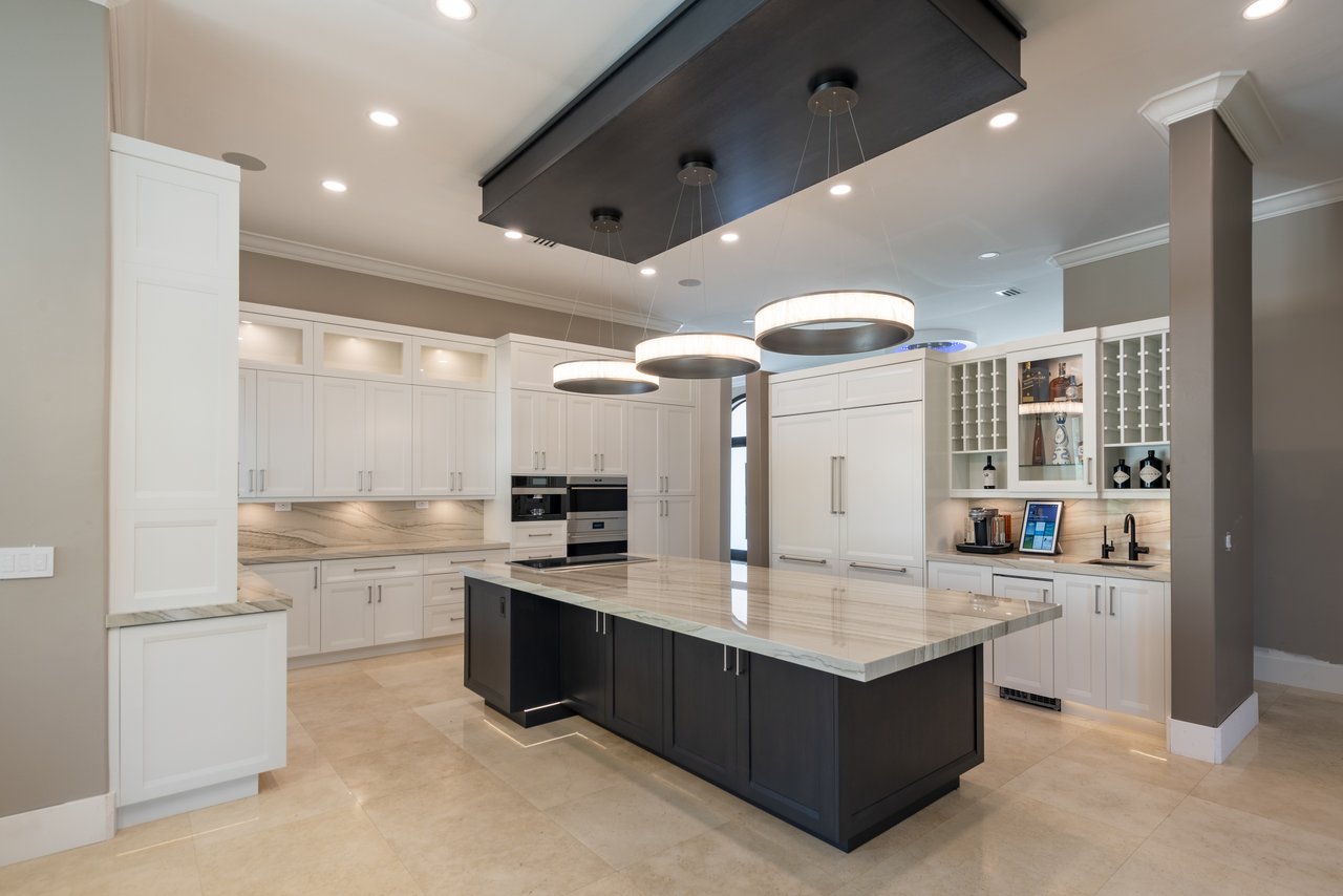 White shaker cabinetry with a dark waterfall-edge quartzite island and a suspended wood ceiling feature over three drum pendants