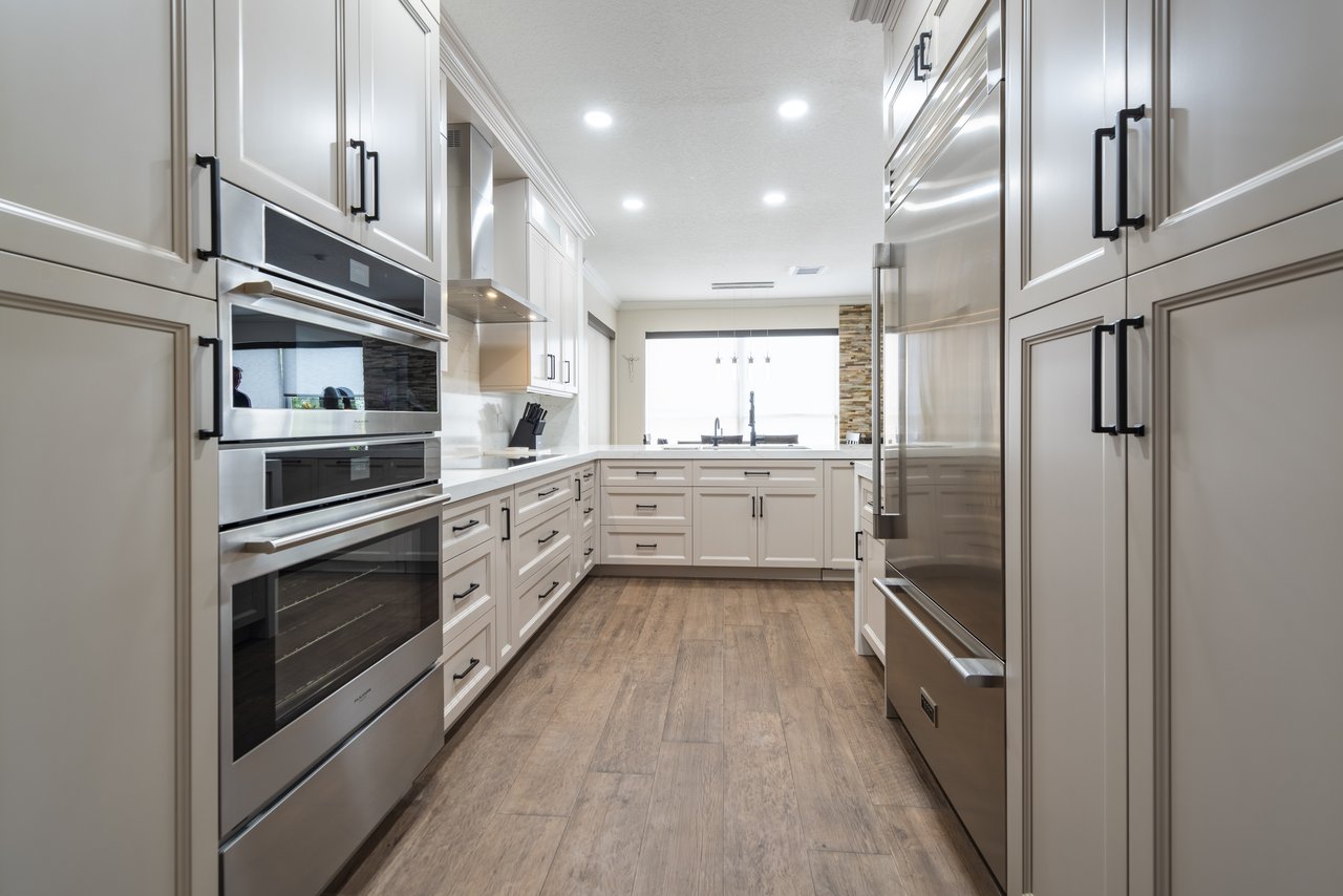White galley kitchen with stainless double wall ovens and a stone backsplash accent