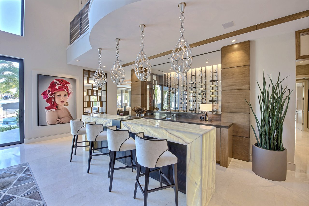 Custom home bar with a backlit onyx waterfall counter, sculptural pendant lighting, and a floor-to-ceiling wine display, fabricated by Wolf in the Woods
