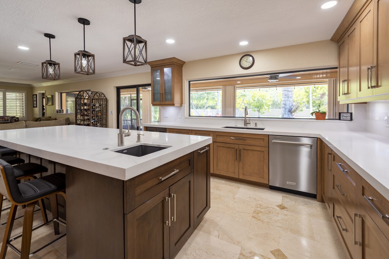 Integrated dishwasher set into maple cabinetry beside a quartz-topped island
