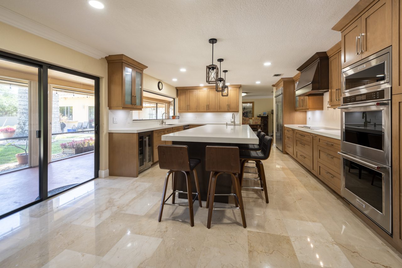 Open maple kitchen with marble flooring, walnut island seating and sliding doors to the patio