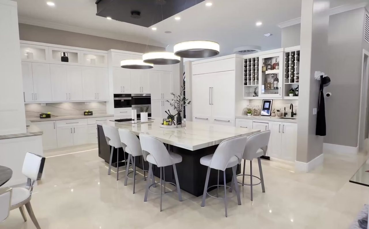 Modern white kitchen with a large stone-topped island seating eight, integrated appliances and a built-in wine display