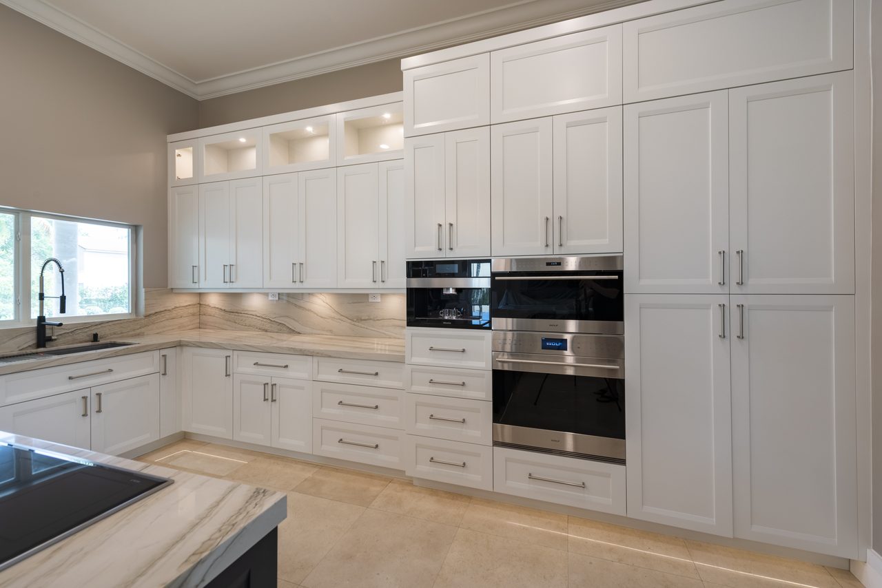 Full-height white cabinetry with built-in wall ovens, coffee system and stone backsplash