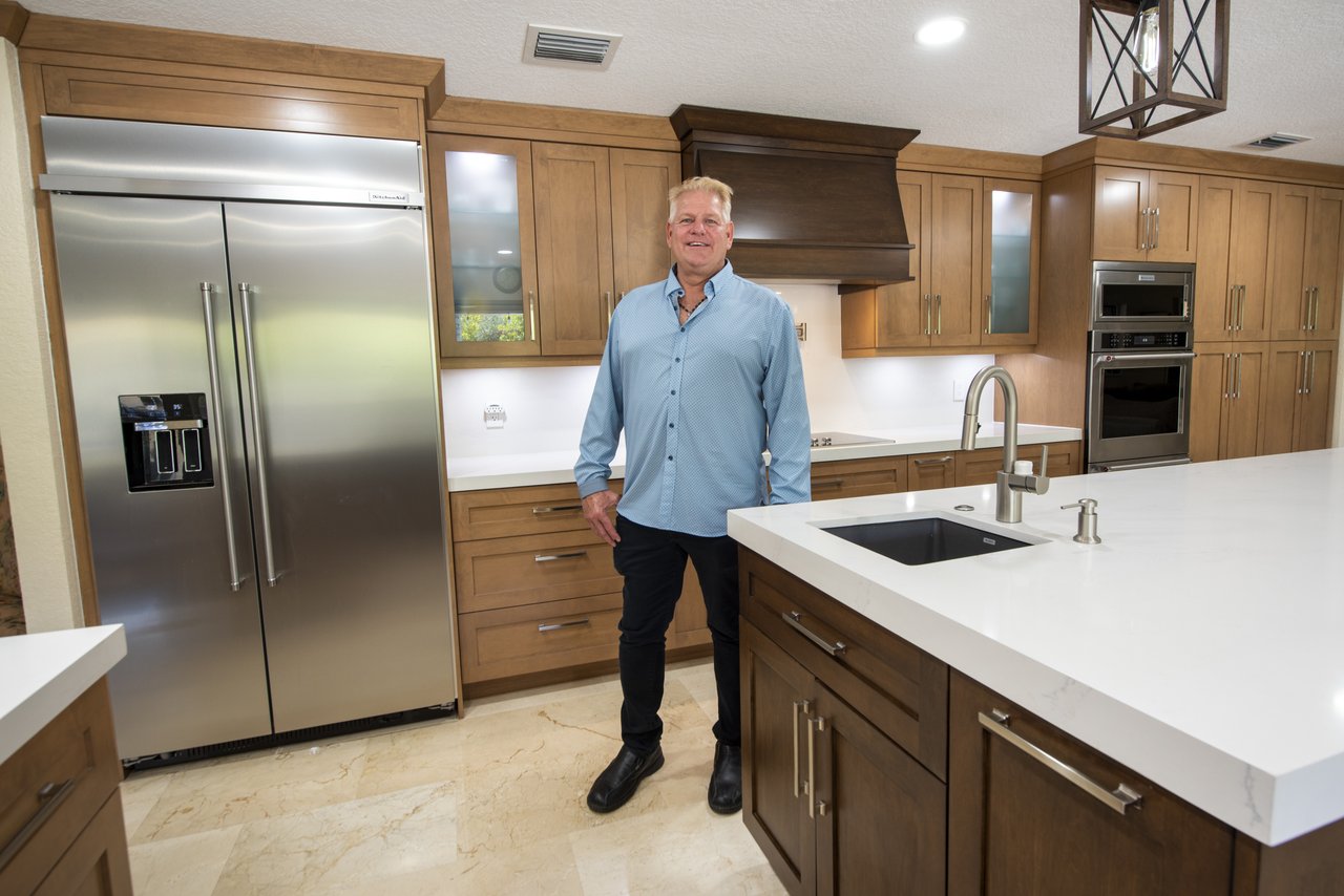 Bill, owner of Wolf in the Woods Design Center, in a completed South Florida kitchen with stainless appliances and warm wood cabinetry